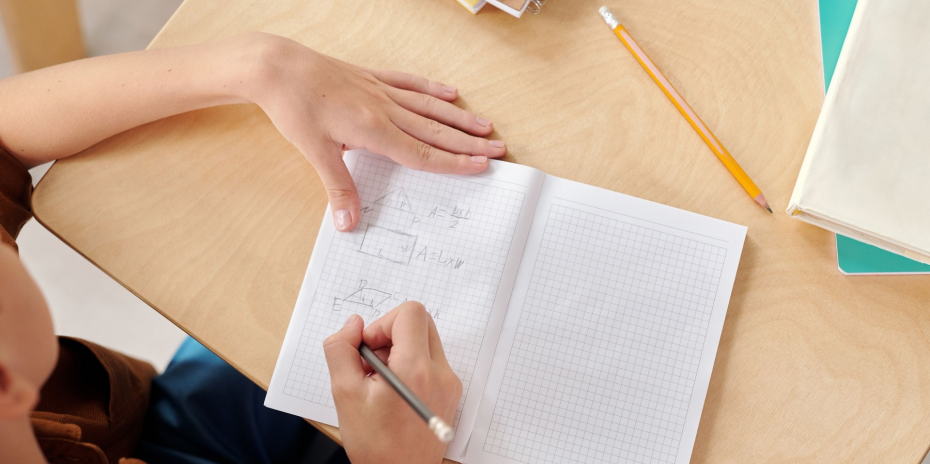 A student writing arithmetic equations in a graph-paper notebook.