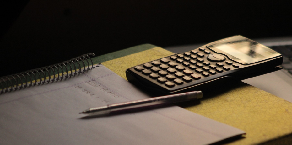 A calculator, pen, and open notebook arranged on a study desk.